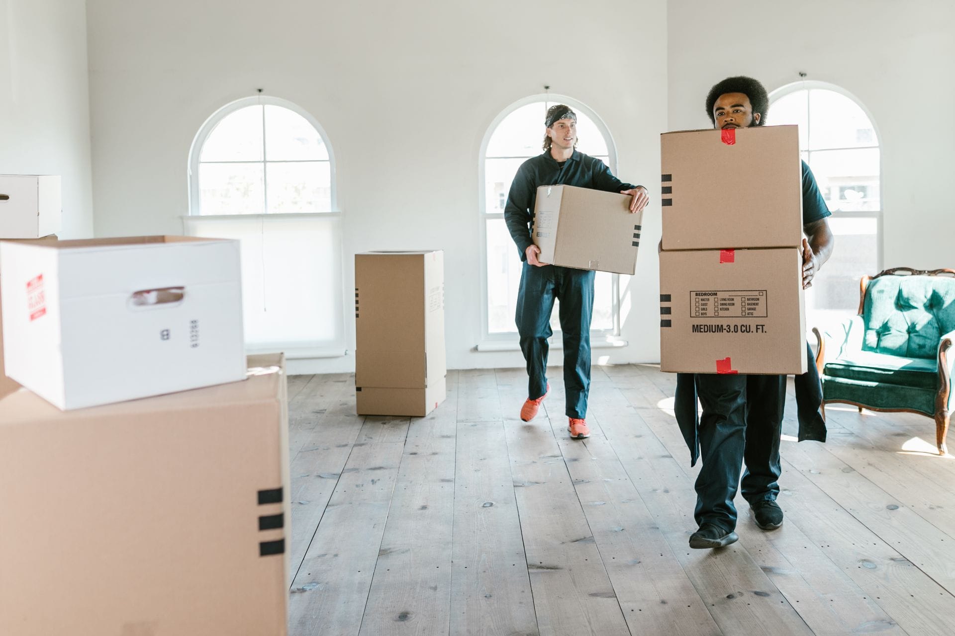 Zwei Umzugshelfer von Move It Easy tragen Kartons durch einen hellen, leeren Raum